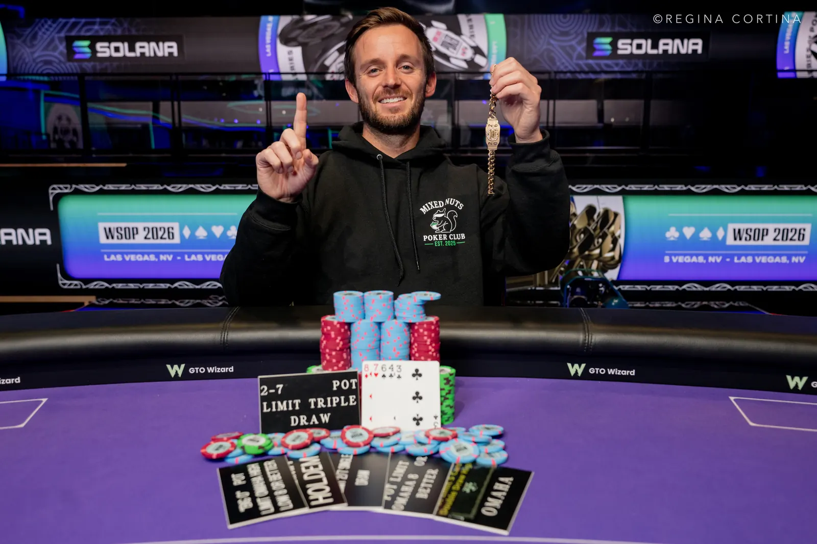 Dylan Smith z uniesioną złotą bransoletą WSOP, uśmiechając się do kamery.