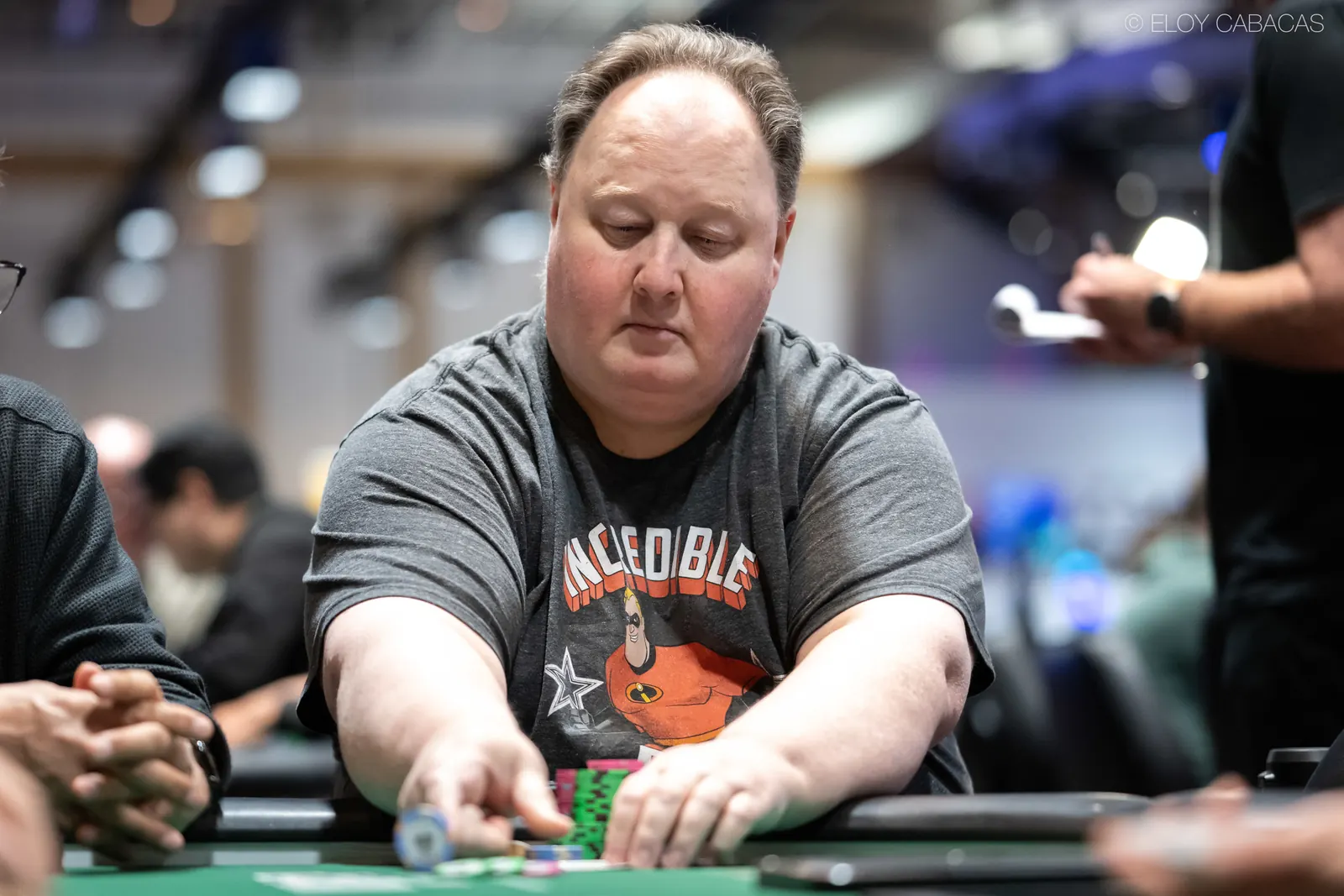 Greg Raymer siedzi przy stole pokerowym, prezentując swoje skamieniałości graczom.