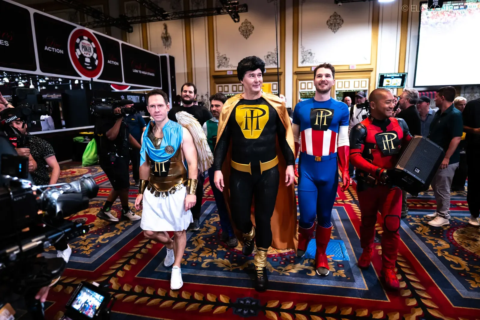 Phil Hellmuth w stroju superbohatera w otoczeniu innych postaci, wchodzący do sali turniejowej WSOP Main Event 2026
